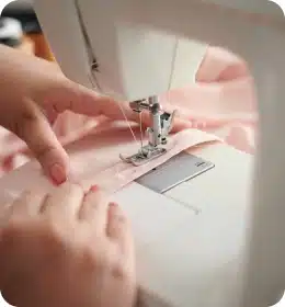 des mains guide le tissu sous le pied de biche d'une machine à coudre