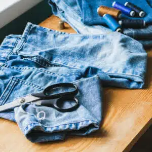 Handicraft, clothing repair. Ripped blue jeans lie on a wooden table. The concept of economical reuse of things. Horizontal frame selective focus