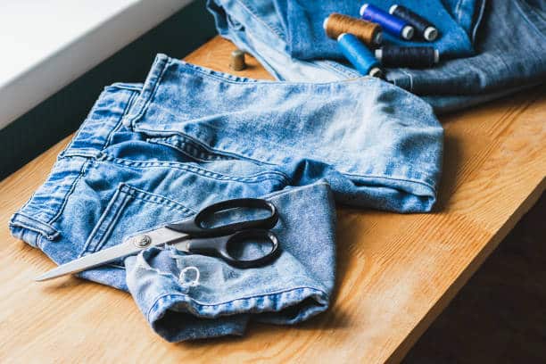 Handicraft, clothing repair. Ripped blue jeans lie on a wooden table. The concept of economical reuse of things. Horizontal frame selective focus