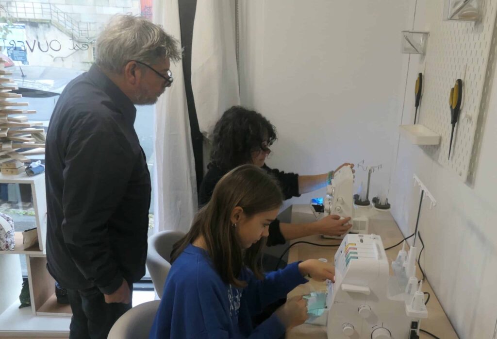 un homme regarde une femme et une jeune fille utiliser des surjeteuses dans l'atelier Re Up Circle à chantenay