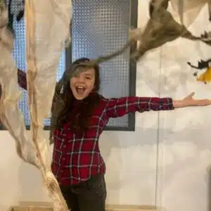 une jeune fille portant des cheveux long et une chemise rouge à carreaux lance des tissus en l'air en faisant un grand sourire