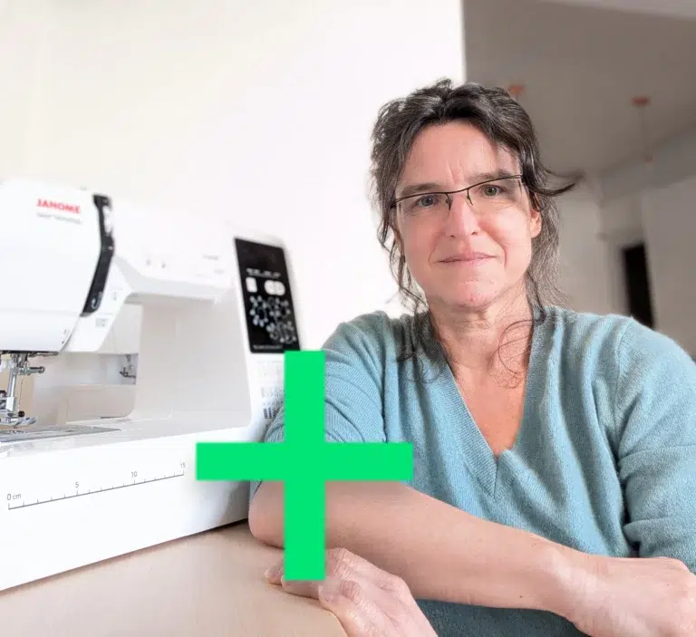 une femme brune souriante posant à côté d'une machine à coudre