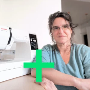 une femme brune souriante posant à côté d'une machine à coudre