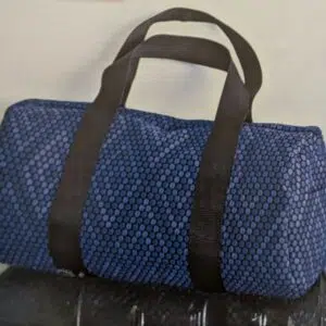 un sac de sport type gymbag (sac circulaire sur les côtés) en jacquard bleu à pois de différentes teintes de bleu qui forment des losanges. le sac a des anses noires