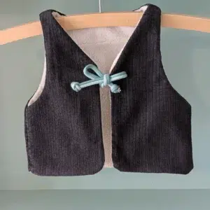 gilet de berger enfant réalisé avec des tissus upcyclés, la face présentée est en velours noir, l'intérieur est en polaire écrue, le lien des deux pans avant est un cordon double avec une partie vert clair et une partie vert plus foncé