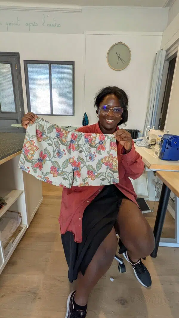 une jeune femme souriante montre le boxer short à motifs floraux qu'elle a réalisé de ses mains lors de la journée couture chez Re Up Circle à Nantes