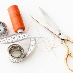 ciseau de couture, bobine de fil orange et mètre ruban blanc