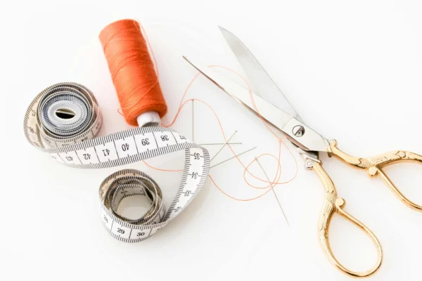 ciseau de couture, bobine de fil orange et mètre ruban blanc